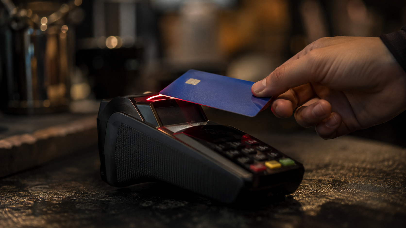 A hand tapping a blue payment card against a card reader terminal, its indicator glowing red